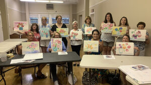 Photograph of about a dozen adult students holding up their class projects from the Victoria Beckert Watercolor Workshop