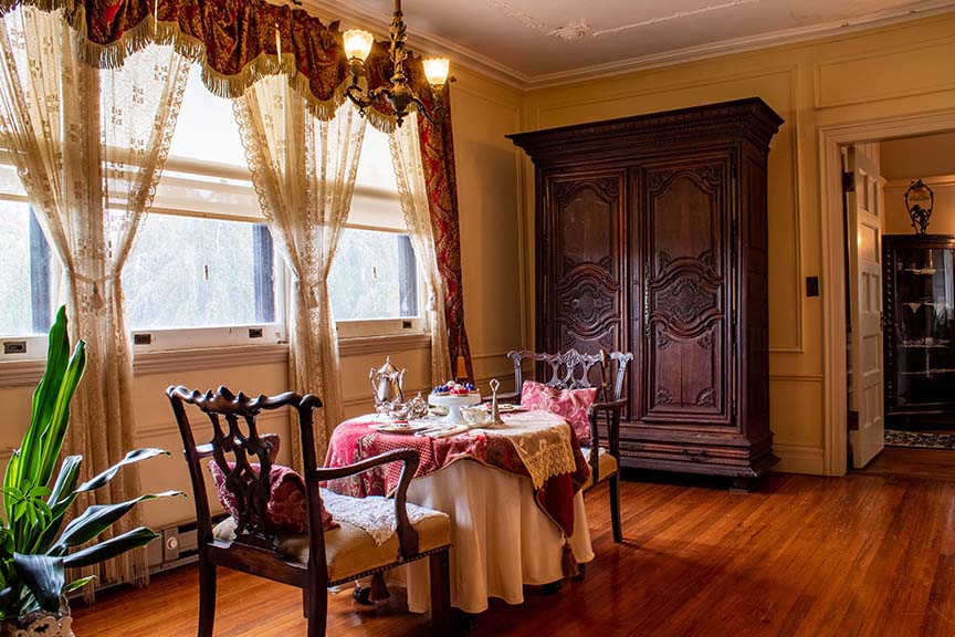 Photograph of inside the Bayard Cutting Arboretum Manor house. This image is of a vintage table set for two that has a plate of sweet treats and a decanter for tea.